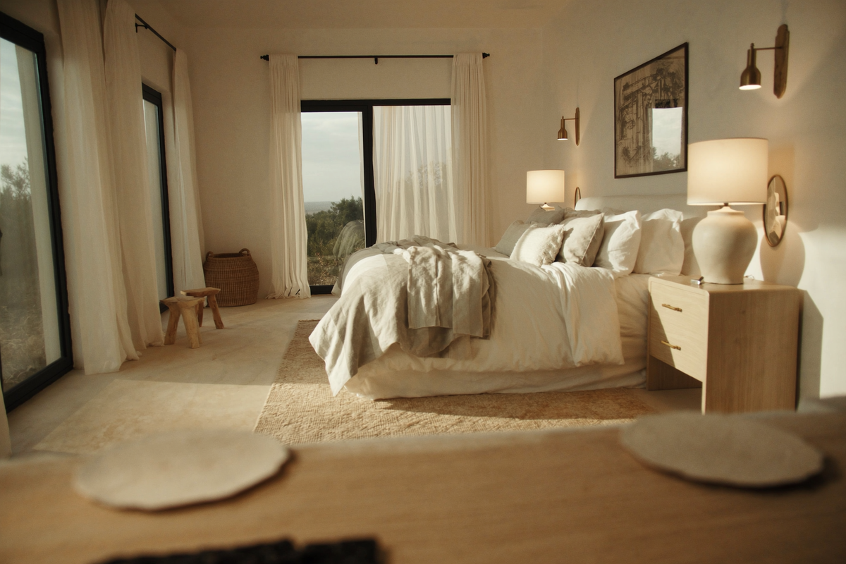 Sunlit bedroom with a bedside lamp and a brass wall sconce above the bed