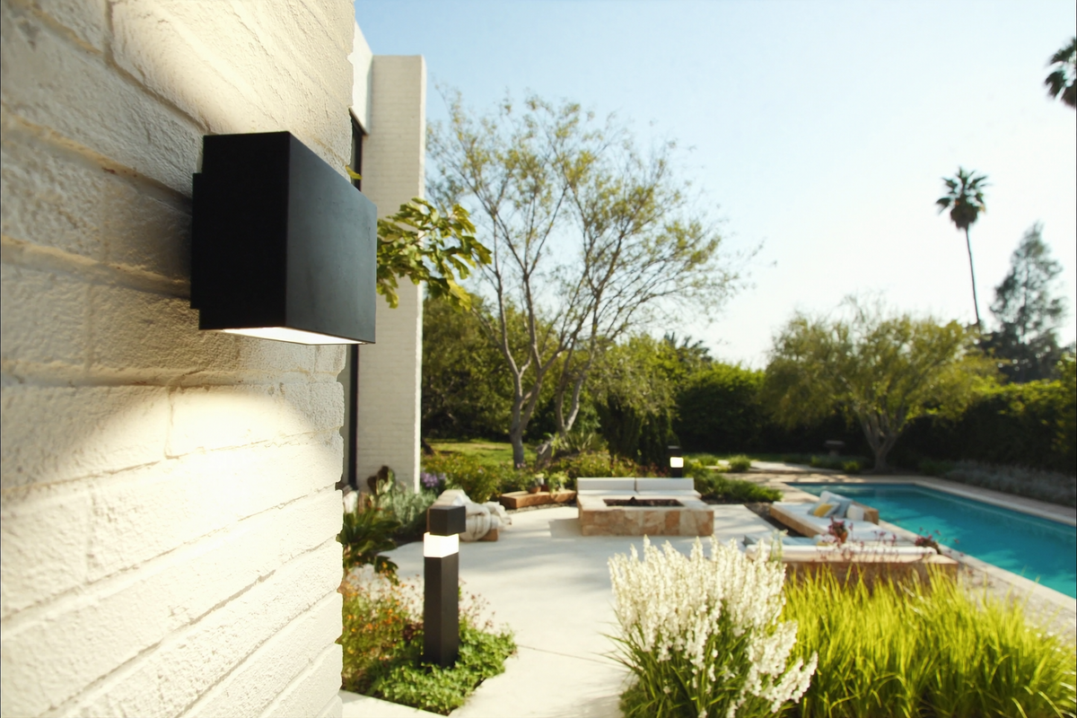 Modern outdoor wall sconce on white brick beside a garden terrace and pool