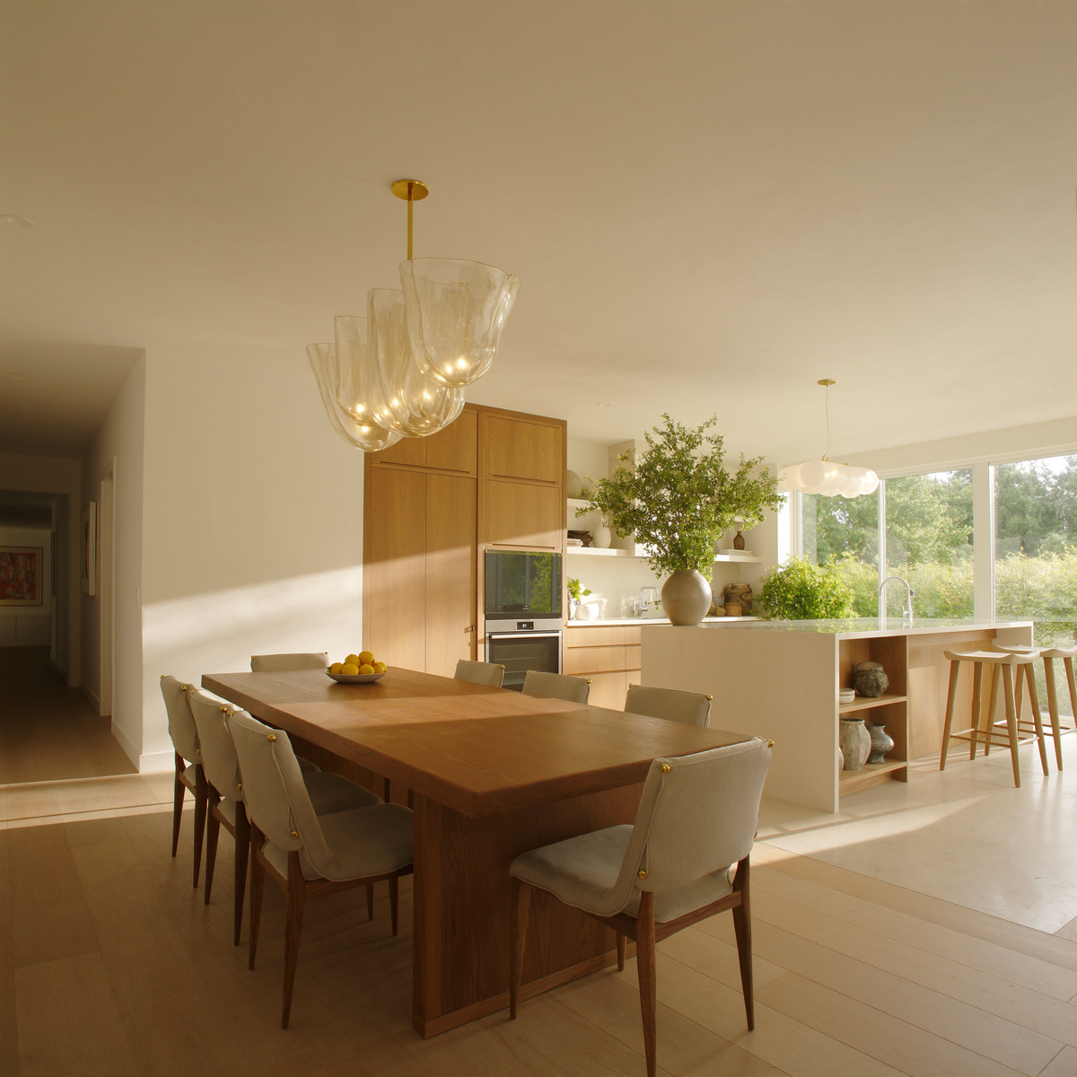 Bright dining room with a sculptural glass pendant over an oak table and open kitchen behind